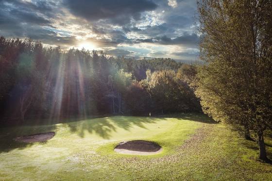 Sunlight breaking through the trees above a green and bunkers at Beamish Park Golf Club