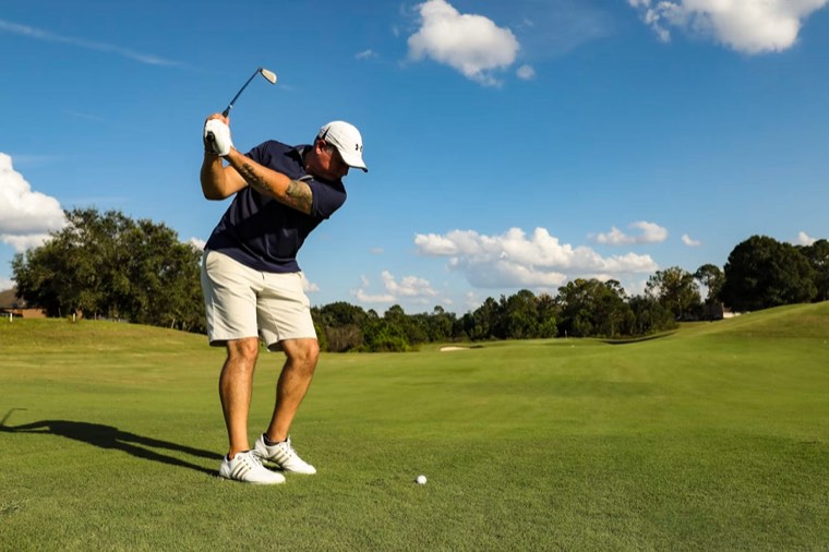 A golfer completing a full swing against a bright sky.