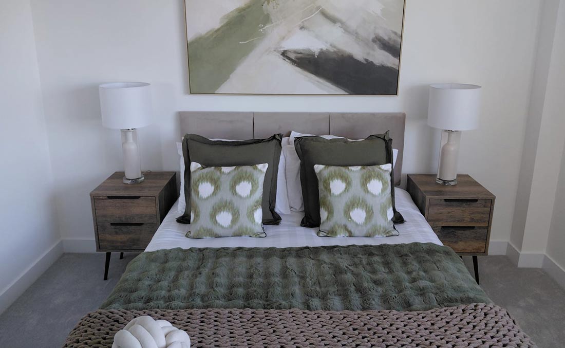 Styled show home bedroom with sage green cushions and throw