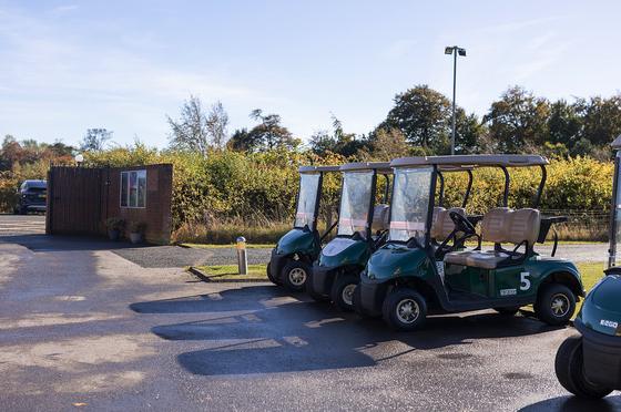 A row of green golf buggies parked outside the clubhouse